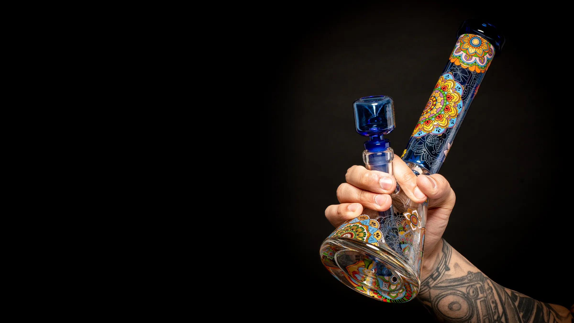 Hand holding a Wormhole Mandala beaker bong against a black background